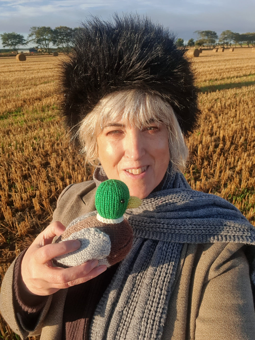 Nicky Stewart bird knitting designer with a knitted duck in a Scottish field of golden corn