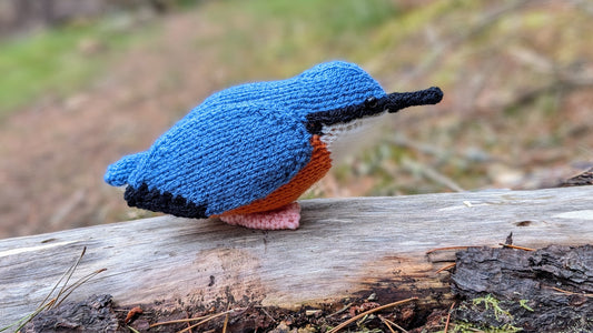 a knitted nuthatch bird sitting on a log in a forest