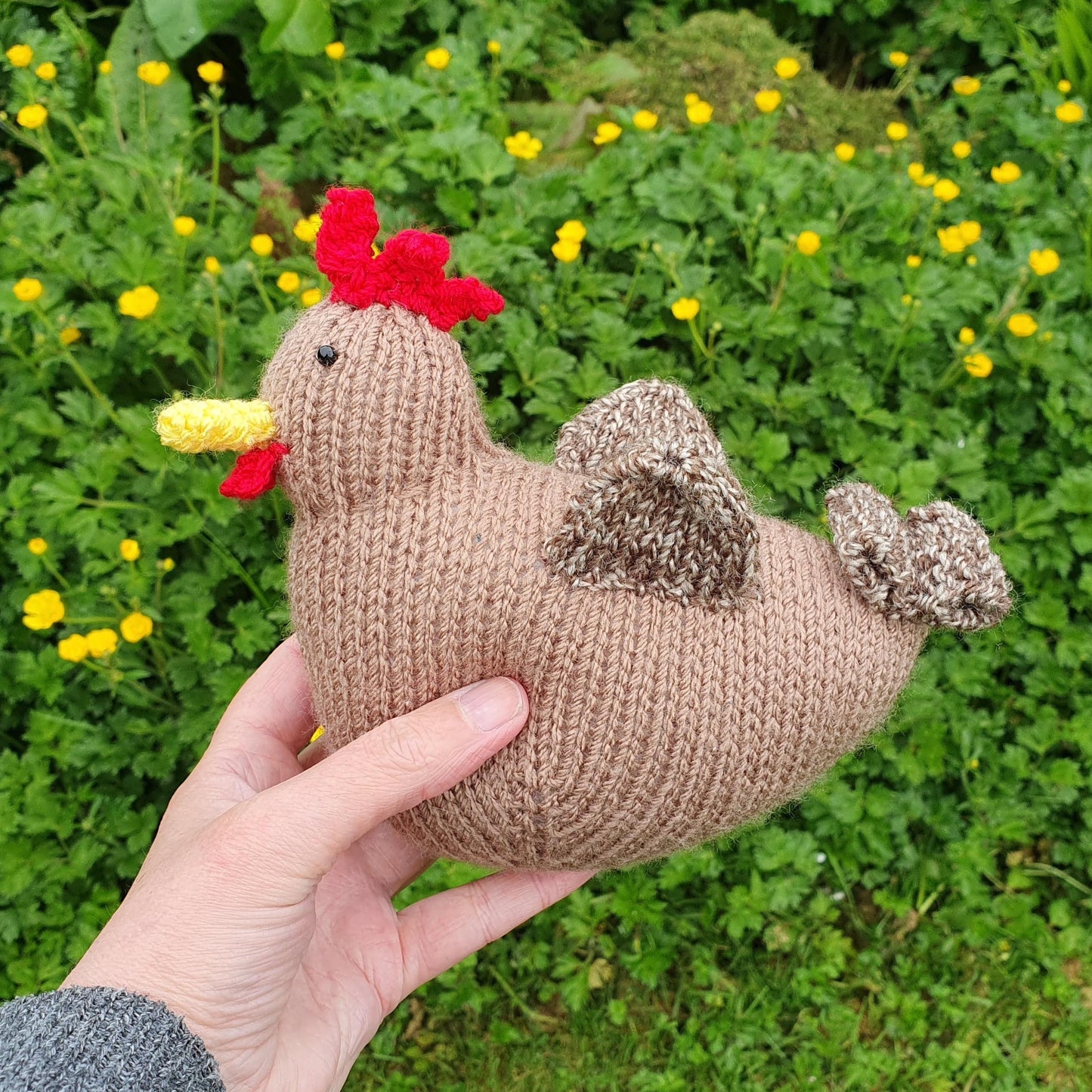 a little brown knitted hen with buttercups in a garden