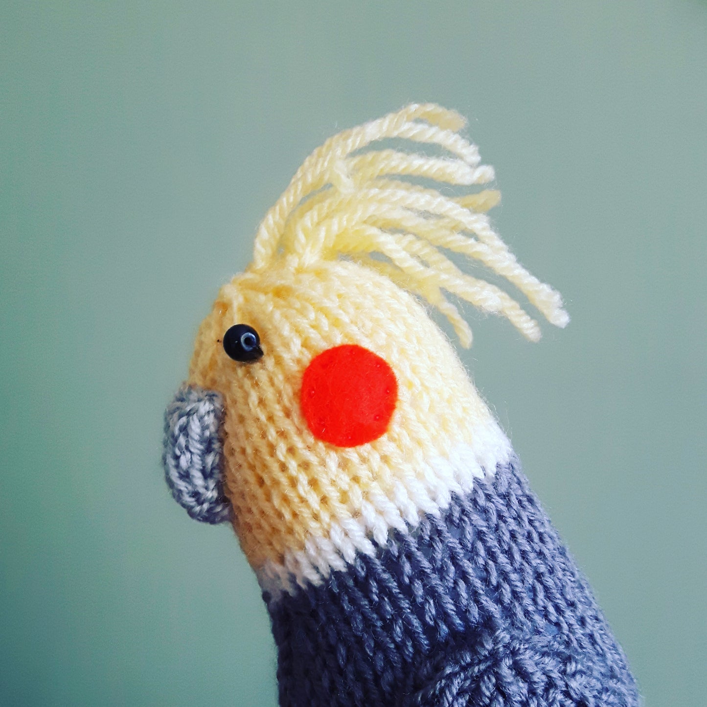 a knitted cockatiel with a yellow head and bright orange cheeks