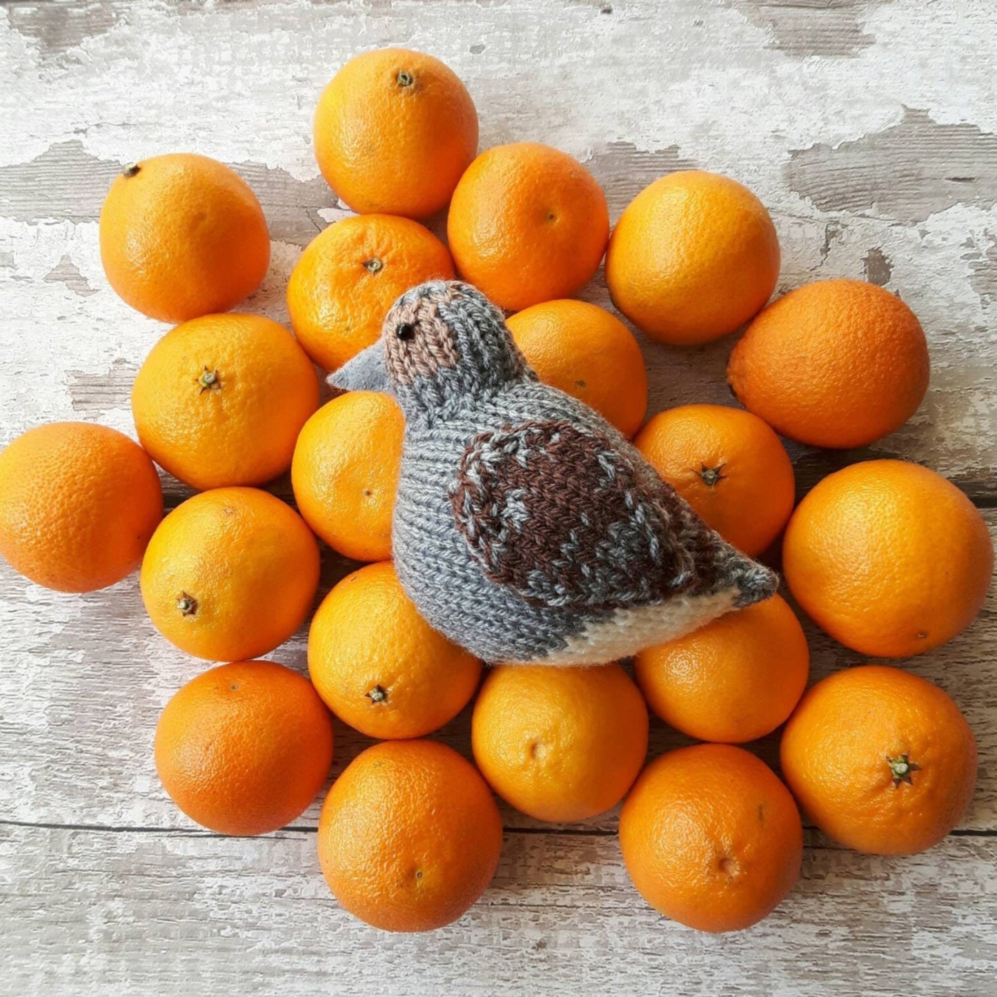 a knitted partirdge is lying on top of a pile of orange satsumas