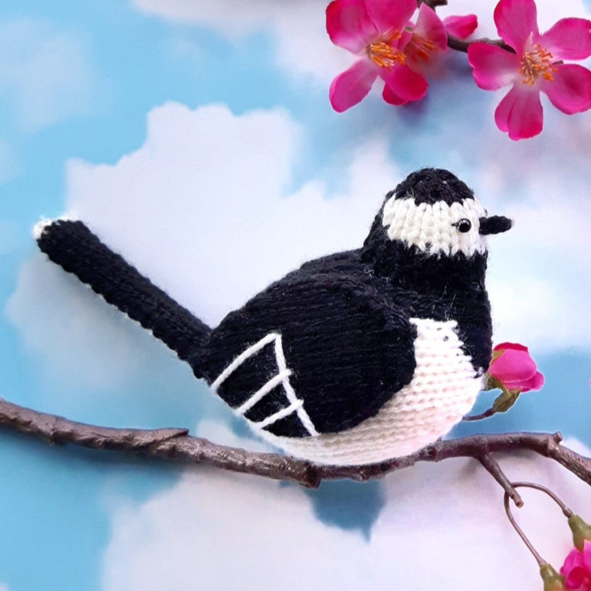 a knitted pied wagtail with pink blossom in the background