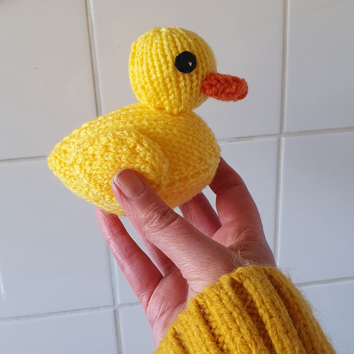 A bright yellow knitted rubber duck being held up in the air by a female wearing a bright yellow jumper.