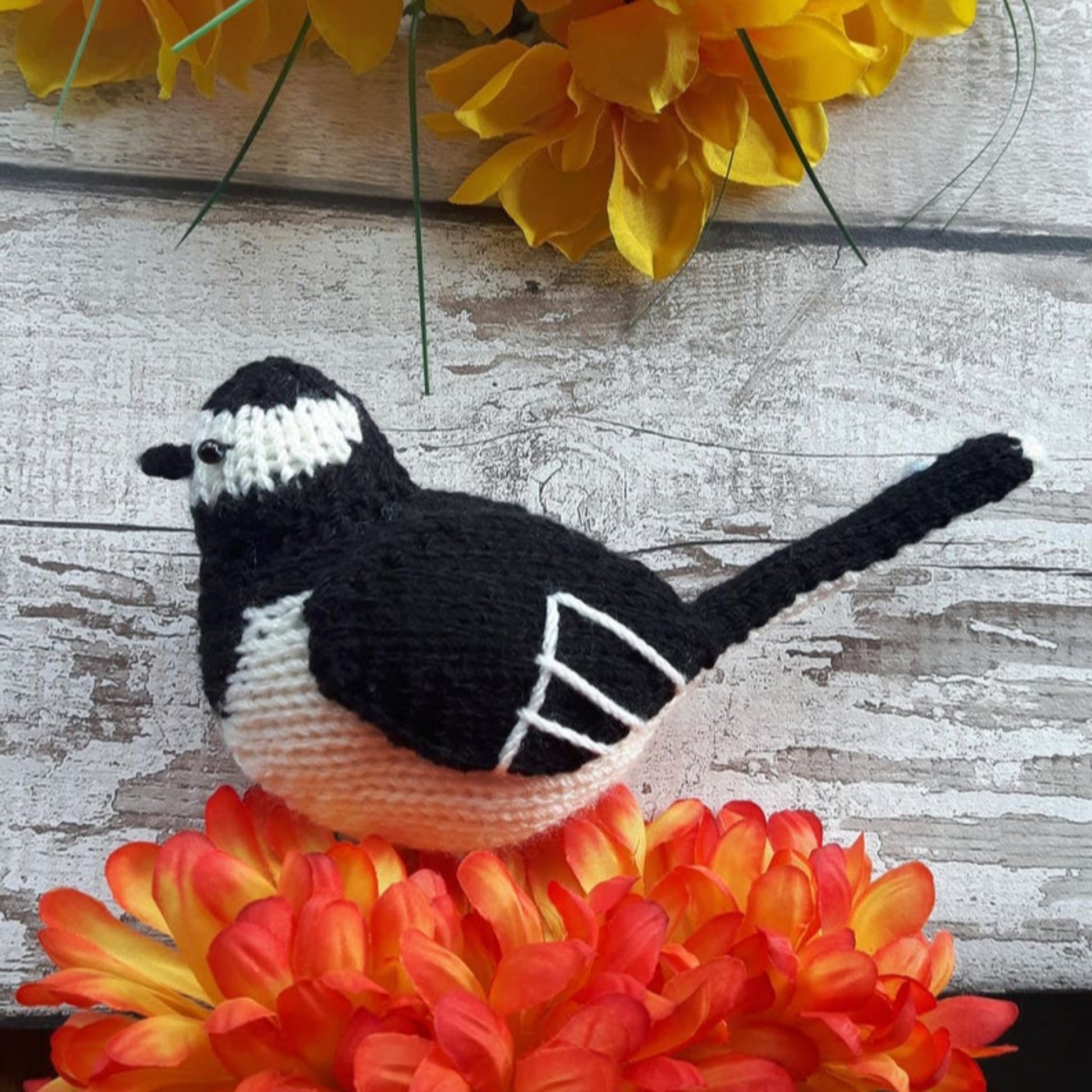 a knitted pied wagtail on a wooden background with luxurious yellow and orange flowers