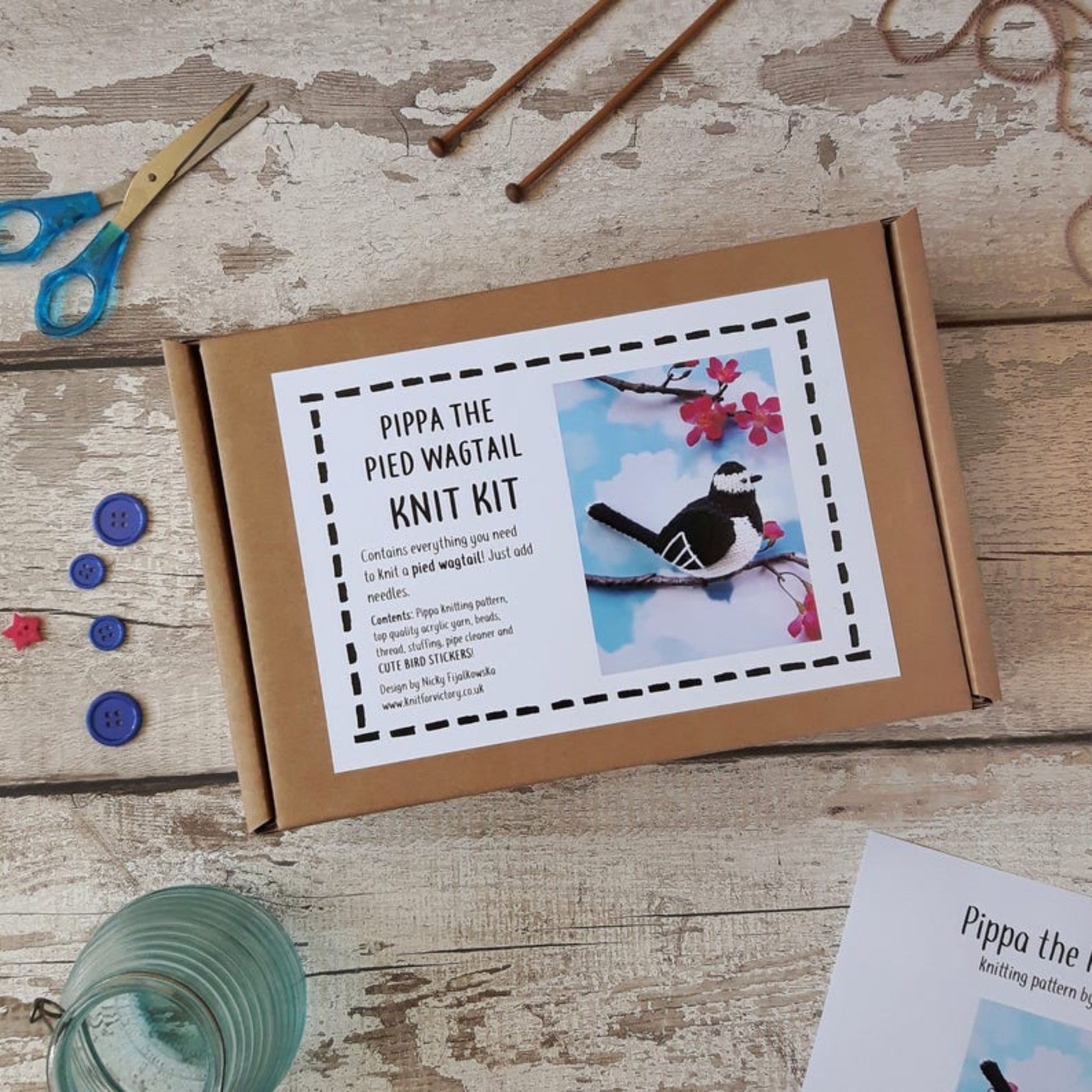 a pied wagtail knitting kit surrounded by knitting needles, scissors, buttons and a glass candle