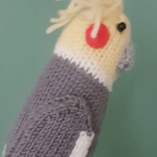 a knitted cockatiel being held against a green background