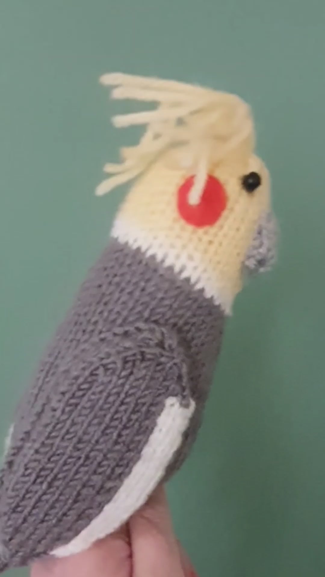 a knitted cockatiel being held against a green background