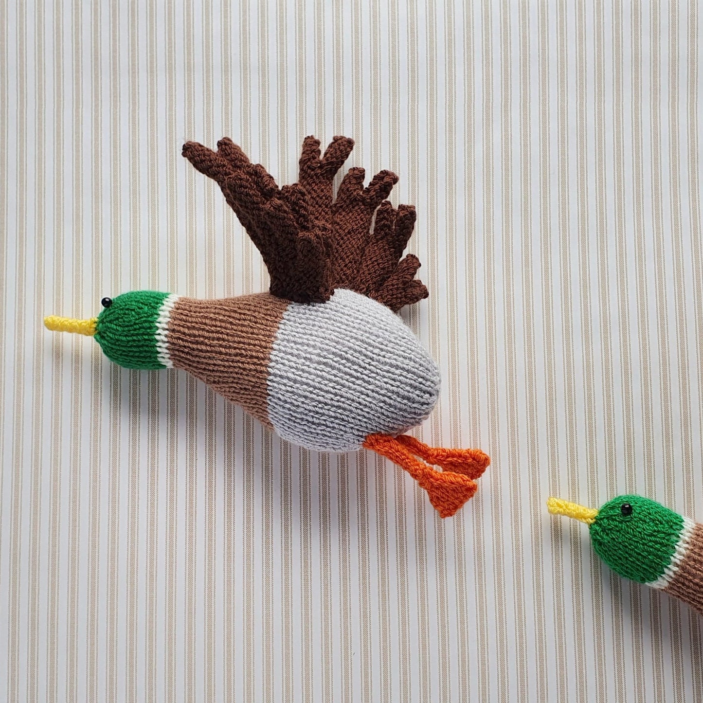 two retro style knitted mallard ducks, flying up a wall which has striped vintage wallpaper