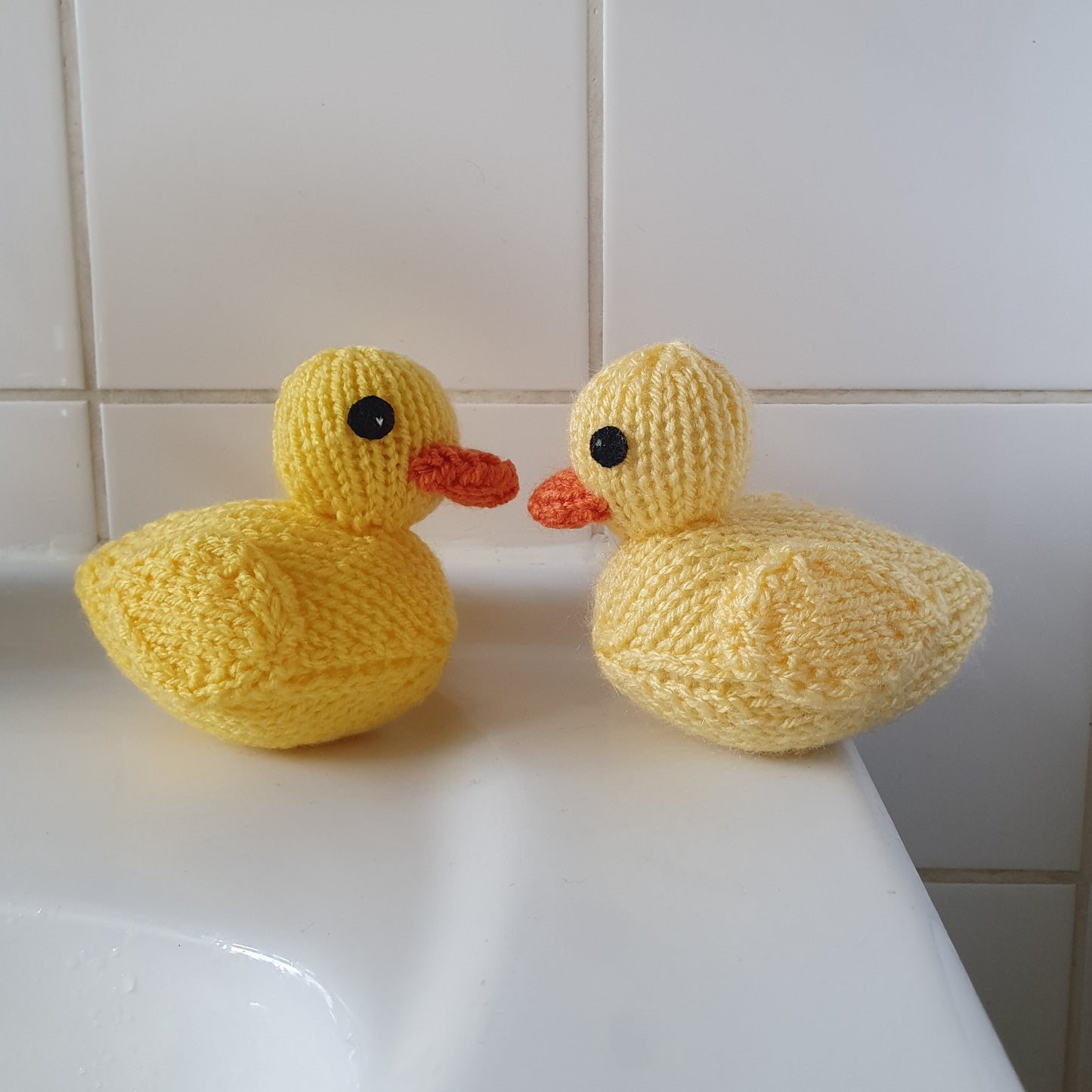 Two yellow knitted rubber ducks sitting next to a sink in a bathroom.